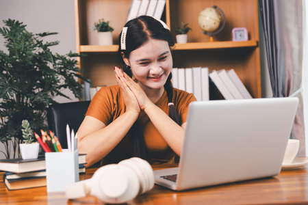 Asian girl doing homework and studying at home. woman using laptop at desk write notes watching webinar, study online, look at learn web class or having virtual call meeting remote working from home.の写真素材