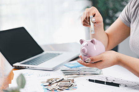 Businesswoman saving money with piggy bank and coins on desk, financial planning and investment concept. Young Asian woman making stack of coin. invest save finance, saving money, investmentの写真素材