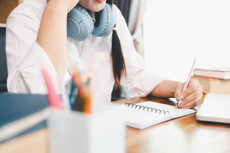 Asian girl student wear headphones learning online watching webinar class looking at laptop computer elearning remote lesson making notes or video calling virtual conference meeting teacher at home.の写真素材