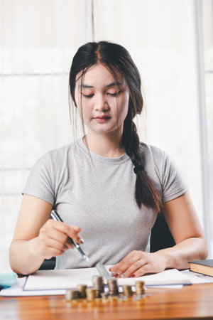 Young Asian woman making stack of coin. invest save finance concept, saving money, investment. dollar bills on table with pile of coins and calculator, money to save and invest to make income.の写真素材