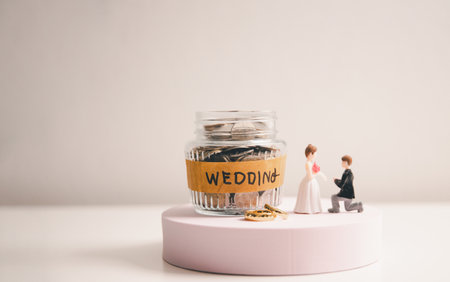 Save money for wedding and planning wedding concept. Sustainable financial goal for family life or married life. Miniature wedding on rows of rising coins, depicts savings or growth for new family.の写真素材
