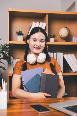 Asian girl doing homework and studying at home. woman using laptop at desk write notes watching webinar, study online, look at learn web class or having virtual call meeting remote working from home.の写真素材