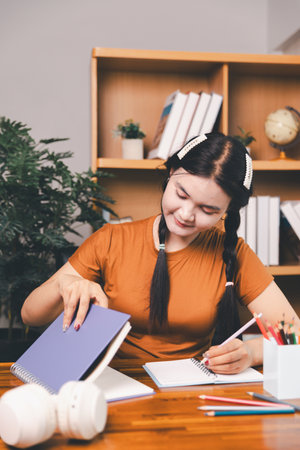 woman sitting at desk working on laptop taking notes in notebook, female studying online, watching webinar using computer, writing check list. Remote college school education, e learning concept.の写真素材