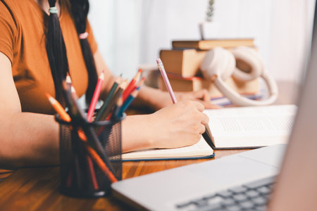 Asian girl doing homework and studying at home. woman using laptop at desk write notes watching webinar, study online, look at learn web class or having virtual call meeting remote working from home.の写真素材