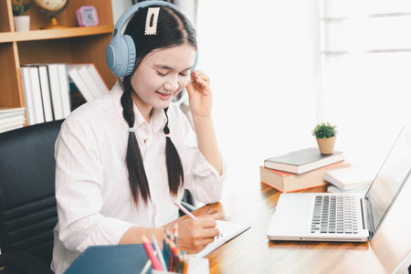 Asian girl student wear headphones learning online watching webinar class looking at laptop computer elearning remote lesson making notes or video calling virtual conference meeting teacher at home.の写真素材