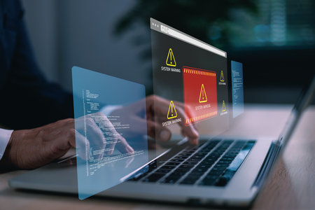 Hands typing on laptop with digital system warning alert on virtual screen, concept of cybersecurity threat, data breach, malware, coding error, online risk, computer failure and IT protection.の写真素材