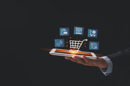 Businessman holding smartphone with glowing virtual shopping cart and ecommerce icons, representing online retail, digital purchasing, mobile commerce, modern technology solutions for business growthの写真素材