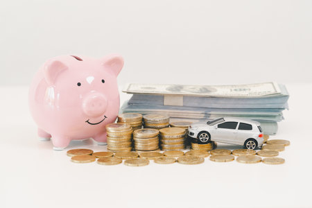 Pink piggy bank with stacked coins, toy car and bundle of dollar bills on white background, representing car savings, down payment cash, auto loan budgeting and purchase planning goals.の写真素材
