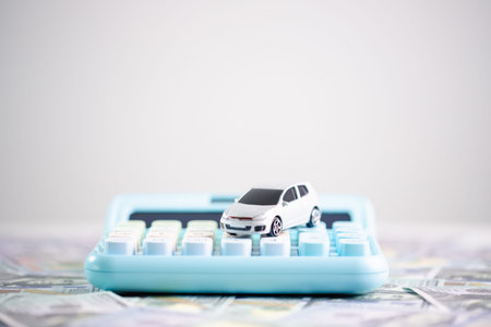 Auto loan budgeting and car purchase planning concept for smart personal finance, featuring small white toy car on blue calculator over scattered banknotes on white background. personal financeの写真素材