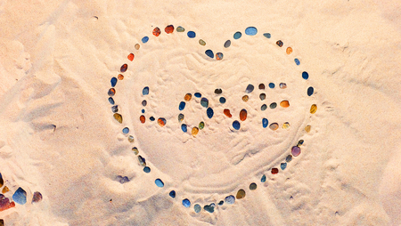 Colorful pebbles on the sand arranged in a heart with the words loveの写真素材