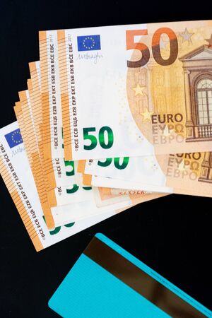 credit card compared with several 50 euro notes. Payment comparison concept. view from above black background.の写真素材