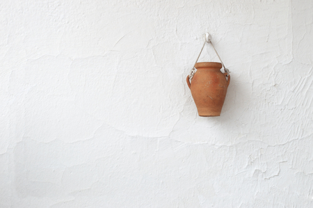 Typical white country house wall in a Mediterranean village with a clay handmade vase hanging from a hock. Empty copy space for editor's text.の写真素材
