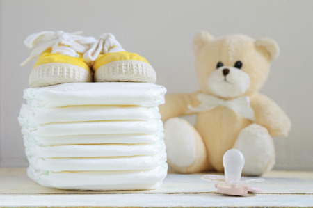 Some nappies on a white wooden table. Sneakers, a pacifier and a teddy bear. Empty copy space for editor's text.の写真素材
