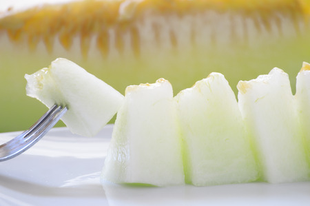 Some cantaloupe pierced with a fork and served on a white plate.の写真素材