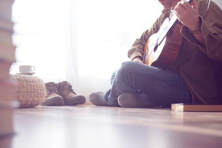 Young man playing the guitar sitting on the parquet floor in the living room. Empty space for copy editor's text.の写真素材