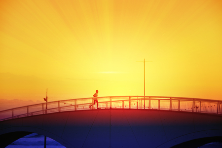Running Man crossing a bridge next to the beack at sunset. Empty copy space for Editor's text.の写真素材