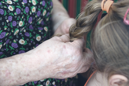 Grandmother hairdressing hand making a pigtail to her granddaughter. Family scene and generation concept.の写真素材