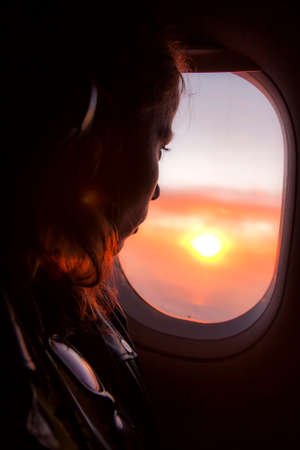 Girl looks at the sun through a window on an airplaneの写真素材