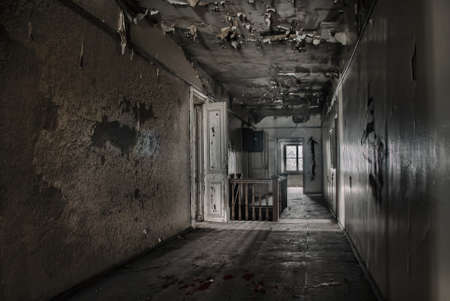 Dark gloomy corridor in an old abandoned building. Dirty wooden doors. Cracked on the walls. A window in the distance. Gloomy atmosphere.の写真素材
