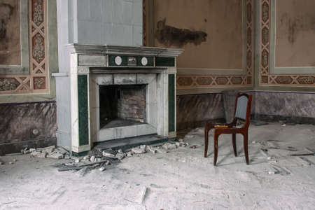An antique fireplace and a chair next to it in an old abandoned manor house. Old shabby and dirty walls. Vintage interior.の写真素材