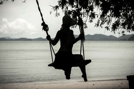 Silhouette of a girl on a swing by the seaの写真素材