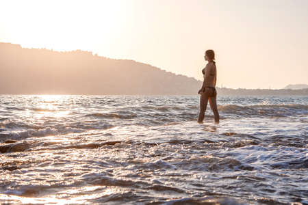 A girl stands on the sea coast in the evening