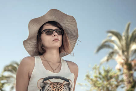 Summer portrait of a girl on a background of palm trees and blue skyの写真素材