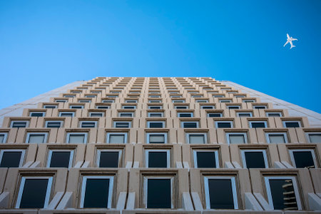 Tall building on a background of blue sky with a flying aircraftの写真素材