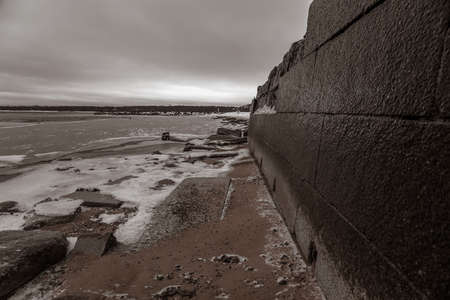 An old granite embankment near the frozen sea. Beautiful winter day. Cloudy sky and snow.の写真素材