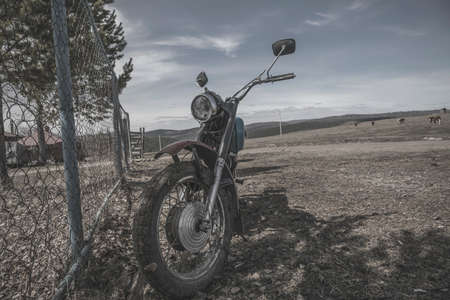 An old abandoned motorcycle stands by the fence. Beautiful nature. Abandoned old technology. Abandoned bikeの写真素材