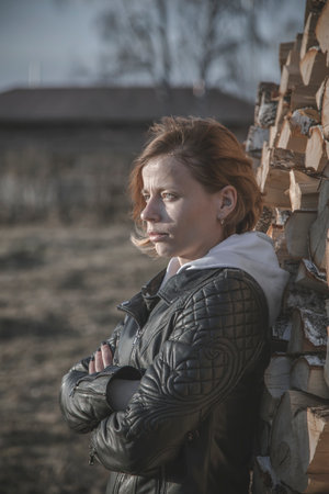 A beautiful girl stands with her back to the wood. Rural landscape. Portrait of a girl in the village.の写真素材
