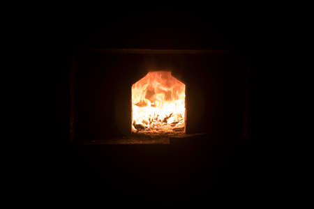 A bright orange fire burns in the stove. Dark background. Light from a burning fire.の写真素材