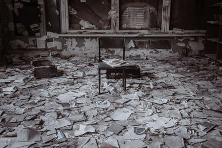 An old abandoned library. Lots of books on the floor. A ray of light from the window. A chair in the middle of the room. Scary old abandoned library.の写真素材
