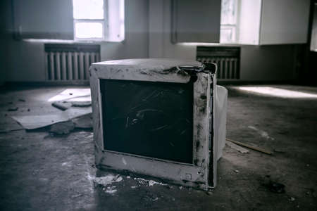 An old, broken monitor lies on the floor in an abandoned building. Sunbeams in the windows in the background. An old room in an abandoned house. Broken monitor.の写真素材