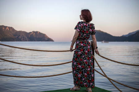 A beautiful girl stands on the beach near the sea. The girl in the sea town. beautiful nature. water and coastline. Sunny evening.の写真素材