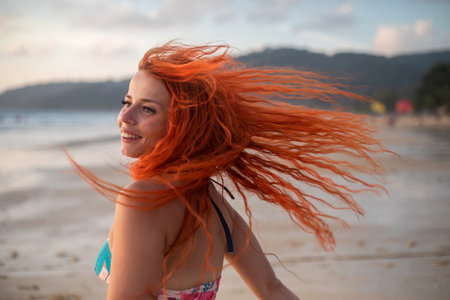 Young woman with long red hair posing on the beach at sunset.の写真素材