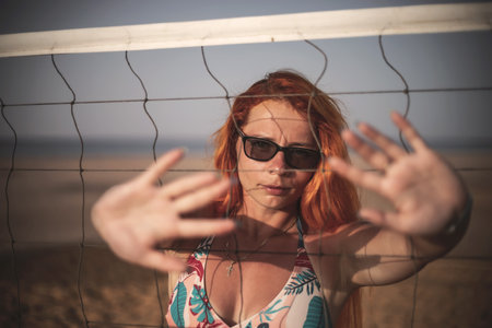 Young redhead woman in swimsuit and sunglasses playing volleyball on the beachの写真素材