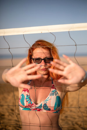 Beautiful young woman in swimsuit and sunglasses playing volleyball on the beachの写真素材