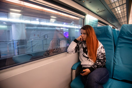 Young redhead woman sitting in a train and looking out the windowの写真素材