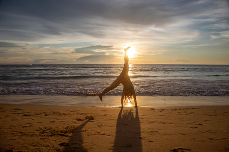 Silhouette of a woman doing yoga on the beach at sunset