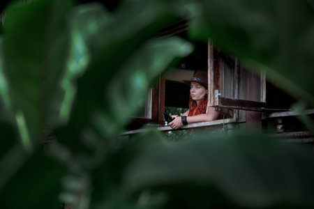 Portrait of a young woman with red hair in a hat sitting in the veranda of a houseの写真素材