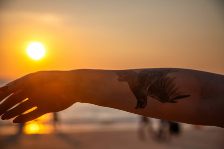 Silhouette of hand with tattoo on the beach at sunset.の写真素材