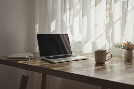 Laptop with blank screen and coffee cup on wooden table in roomの素材