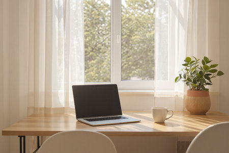 Laptop and coffee cup on wooden table in front of window.の素材