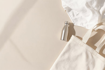 White cotton bag and bottle of water on beige background. Flat lay, top view.の素材