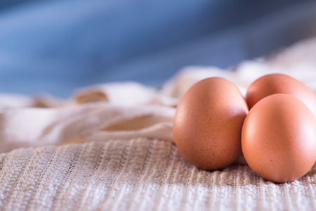 Three farm eggs on a white cloth with a blue background.