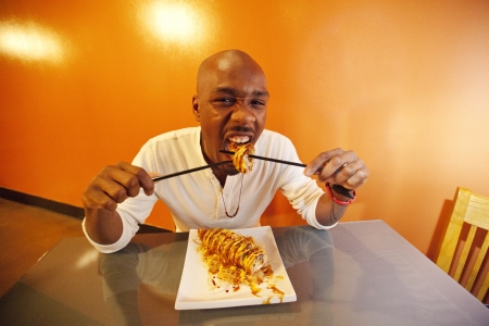 Young African American man playfully eating sushiの写真素材
