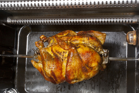 A chicken cooking on a horizontal rotisserie の写真素材