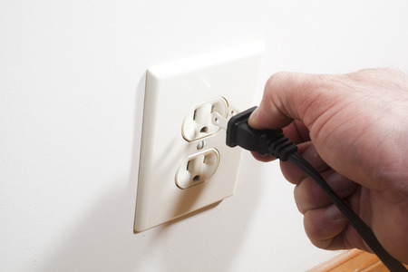 A hand putting a two prong plug into a wall socket 