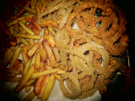 A close up of an assortment of greasy deep fried french fries and onion rings.